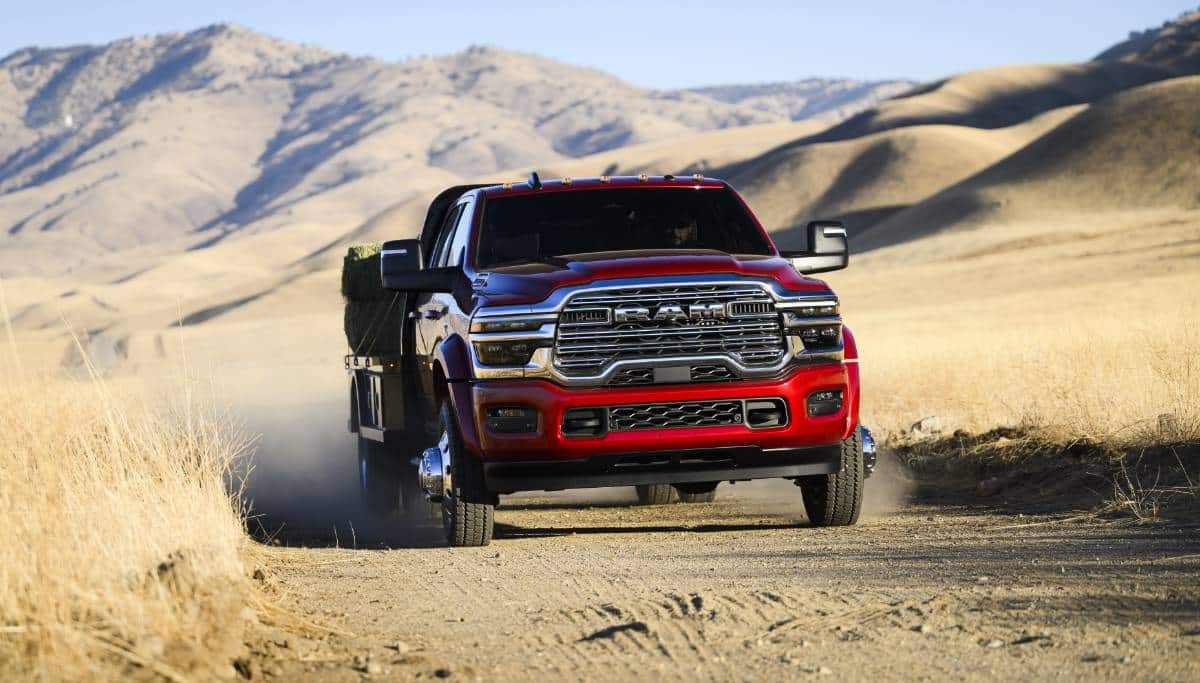 Display A red 2025 Ram 5500 Laramie Chassis Crew Cab carrying several large bales of hay on a long platform upfit as it travels through the desert.