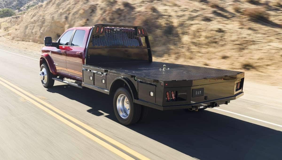 Display A rear angle of a red 2025 Ram 5500 Laramie Chassis Crew Cab with a long platform upfit traveling down a highway.