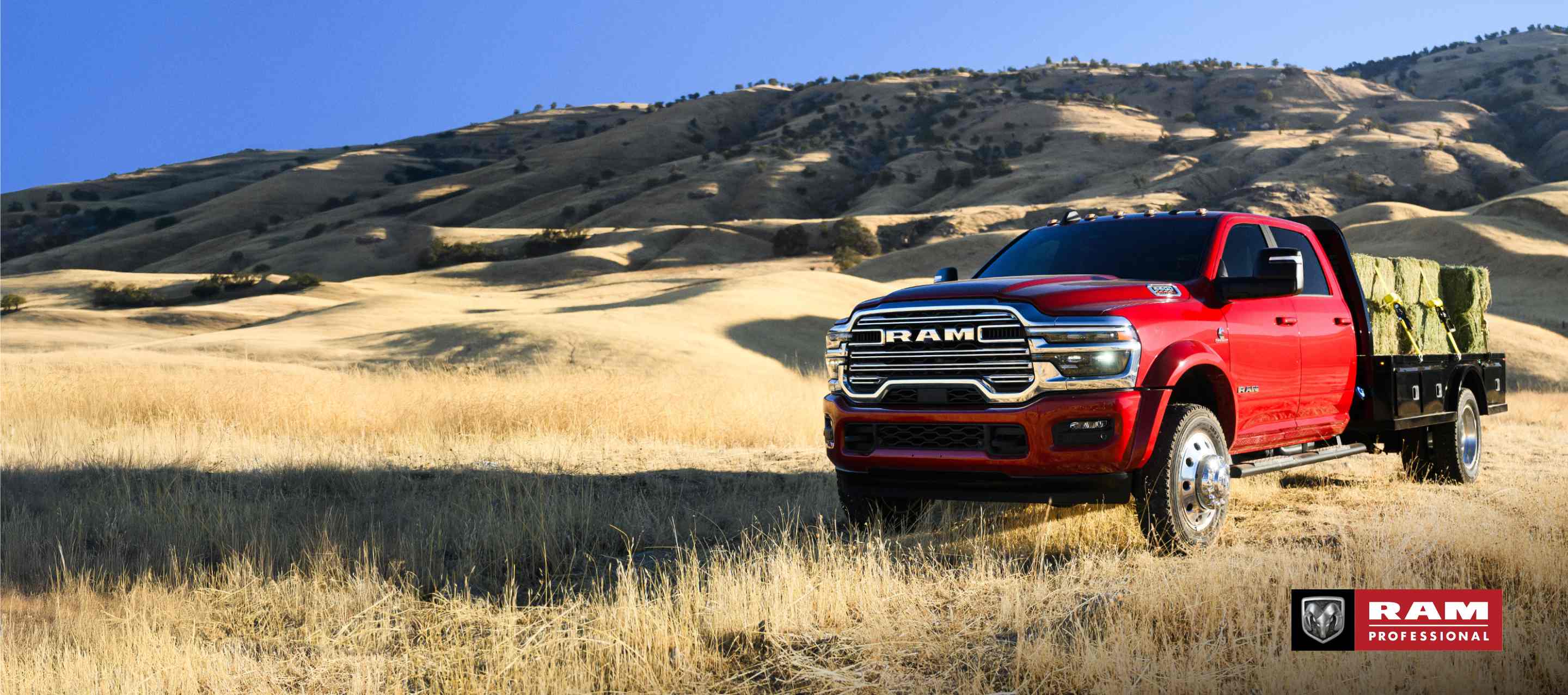 A red 2025 Ram 5500 Laramie Chassis Crew Cab carrying several large bales of hay on a long platform upfit. Ram Professional.