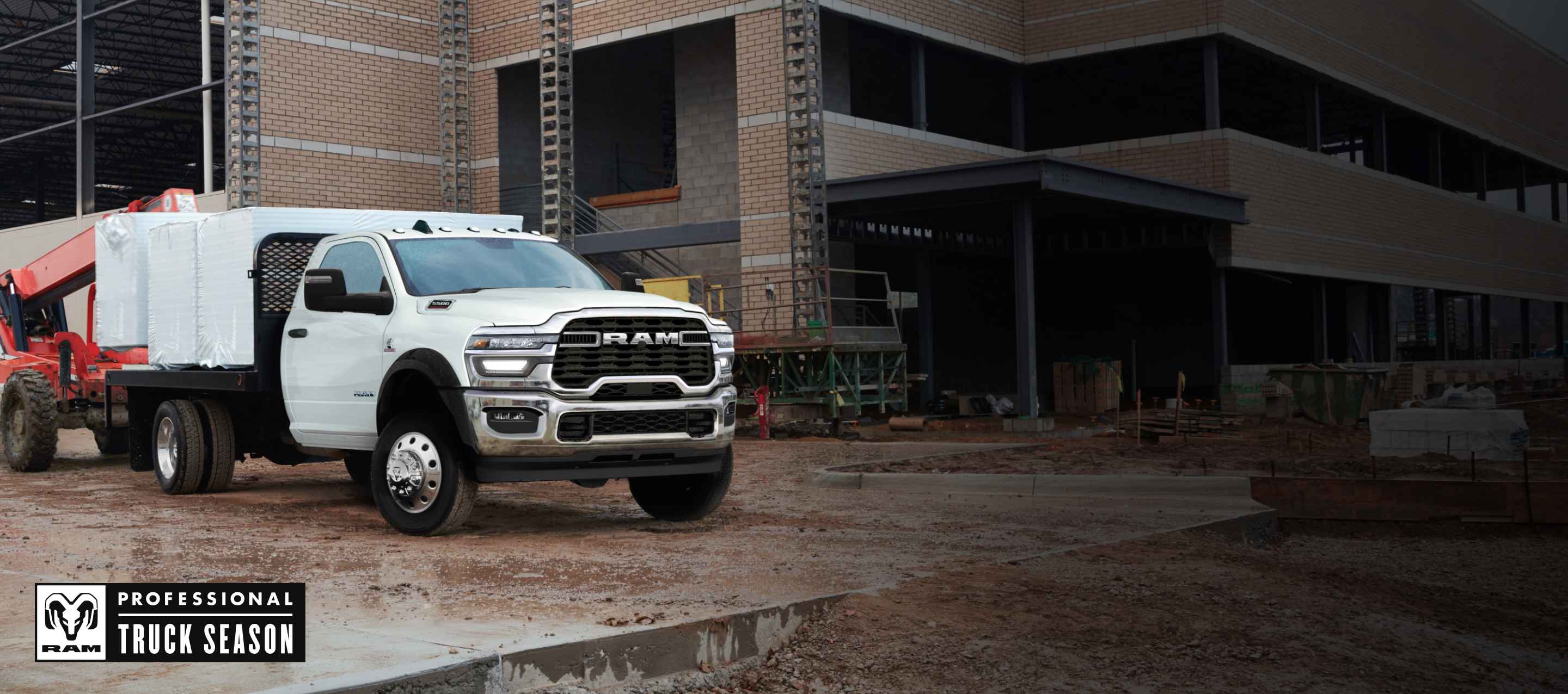 A white 2025 Ram 3500 Big Horn 4x4 Chassis Cab Regular Cab with a platform upfit loaded with building materials, parked at a commercial construction site. Ram Professional Truck Season.