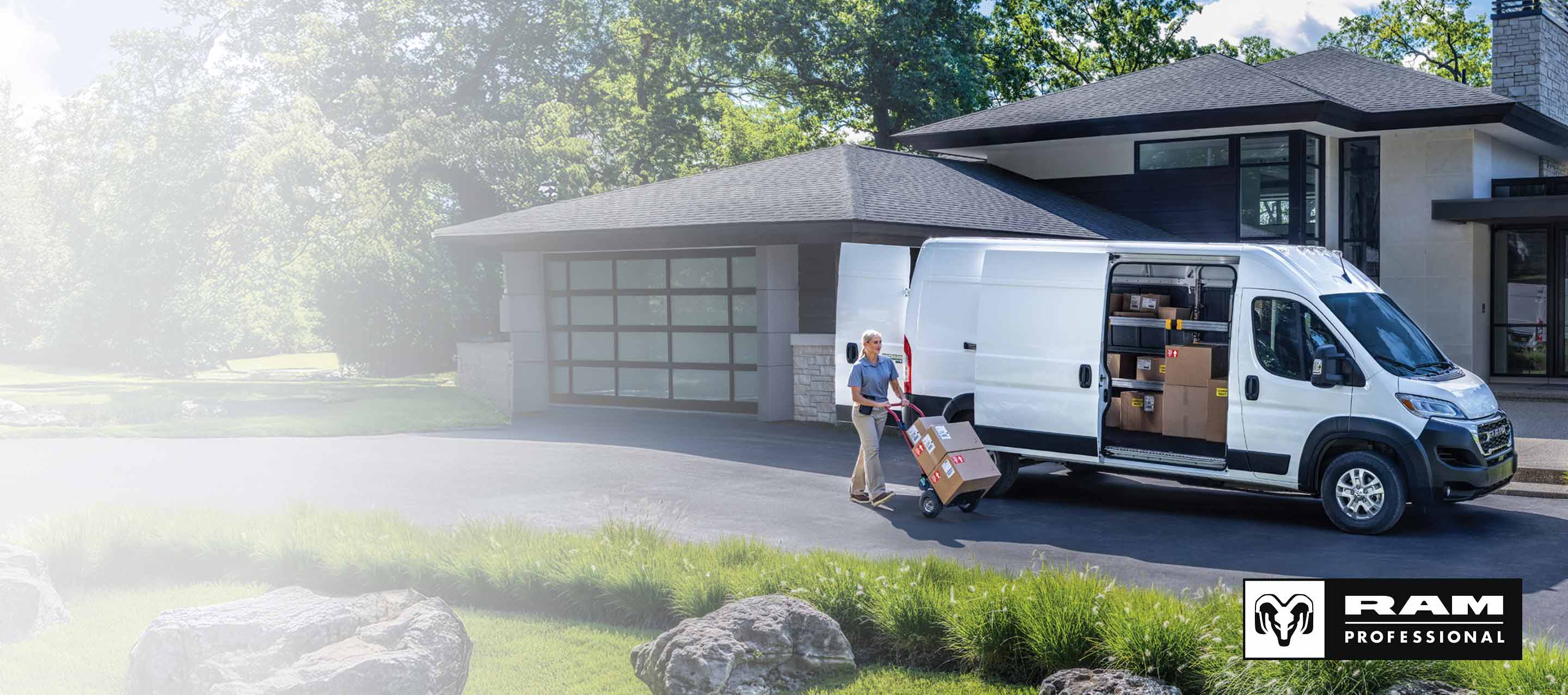 A white 2026 Ram ProMaster EV 3500 SLT High Roof Cargo Van with its passenger-side sliding door and rear doors open, revealing packages inside, parked in the driveway of a neighborhood home, with a delivery person nearby pushing a dolly full of boxes. Ram Professional.