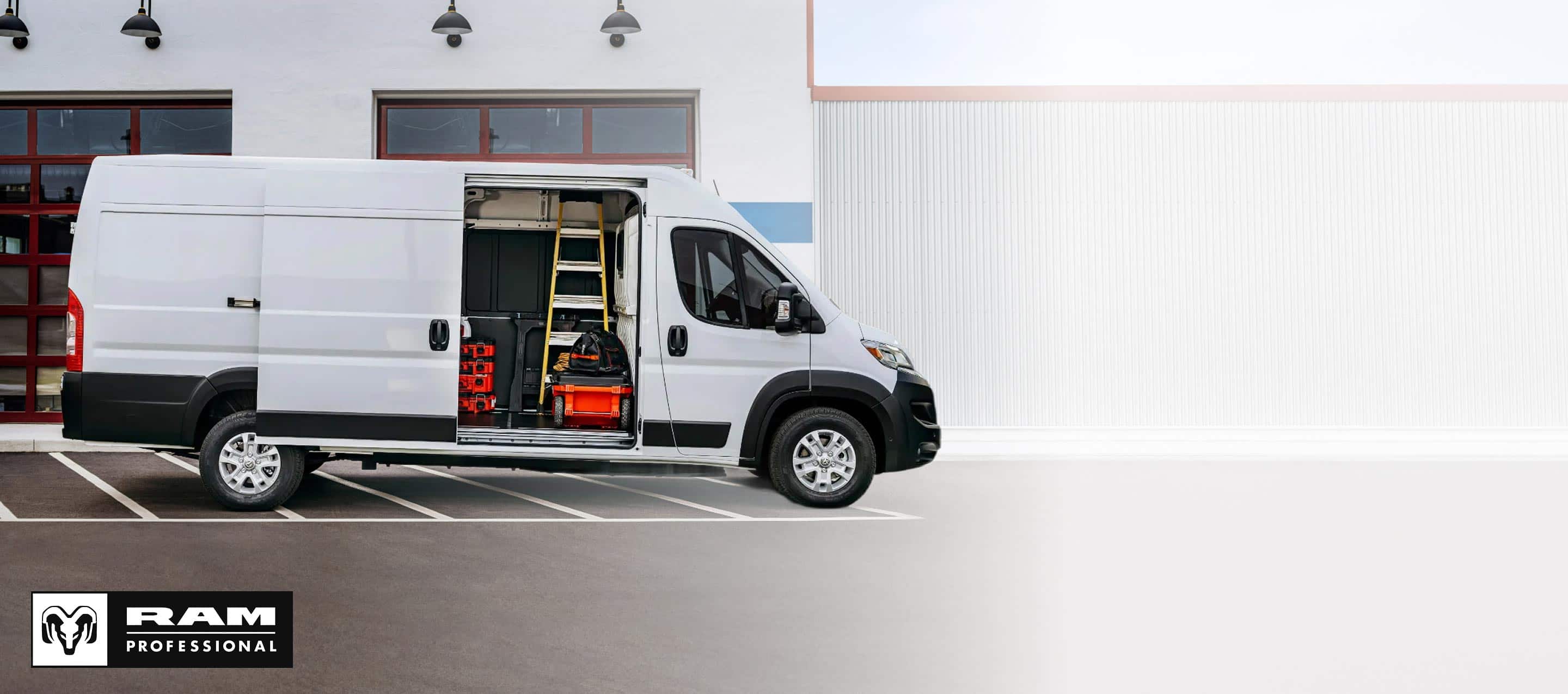 A passenger-side profile of a white 2025 Ram ProMaster EV 3500 SLT High Roof Cargo Van parked beside a commercial garage with its sliding side door open, revealing tools, equipment and a ladder inside. Ram Professional.