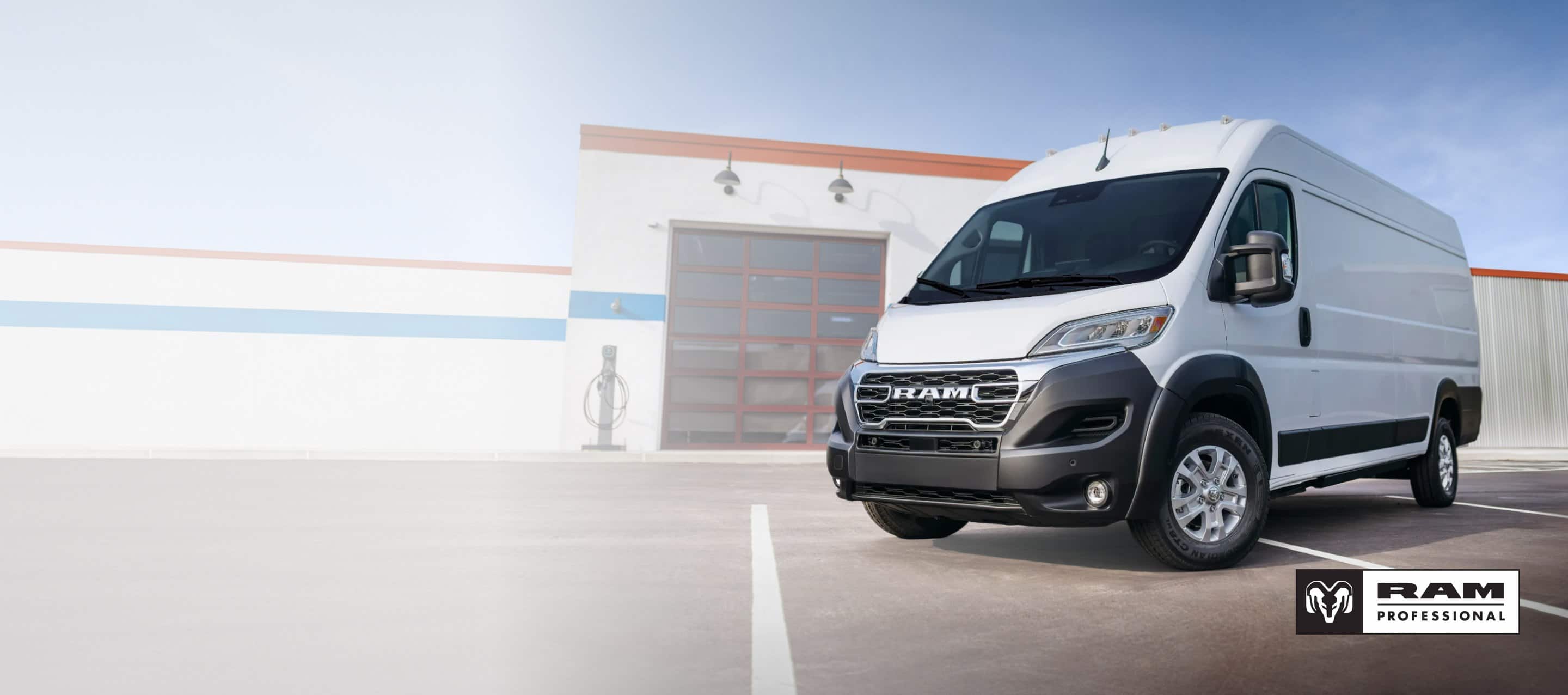 A driver-side front angle of a white 2025 Ram ProMaster EV 3500 SLT High Roof Cargo Van parked near a commercial garage. Ram Professional.