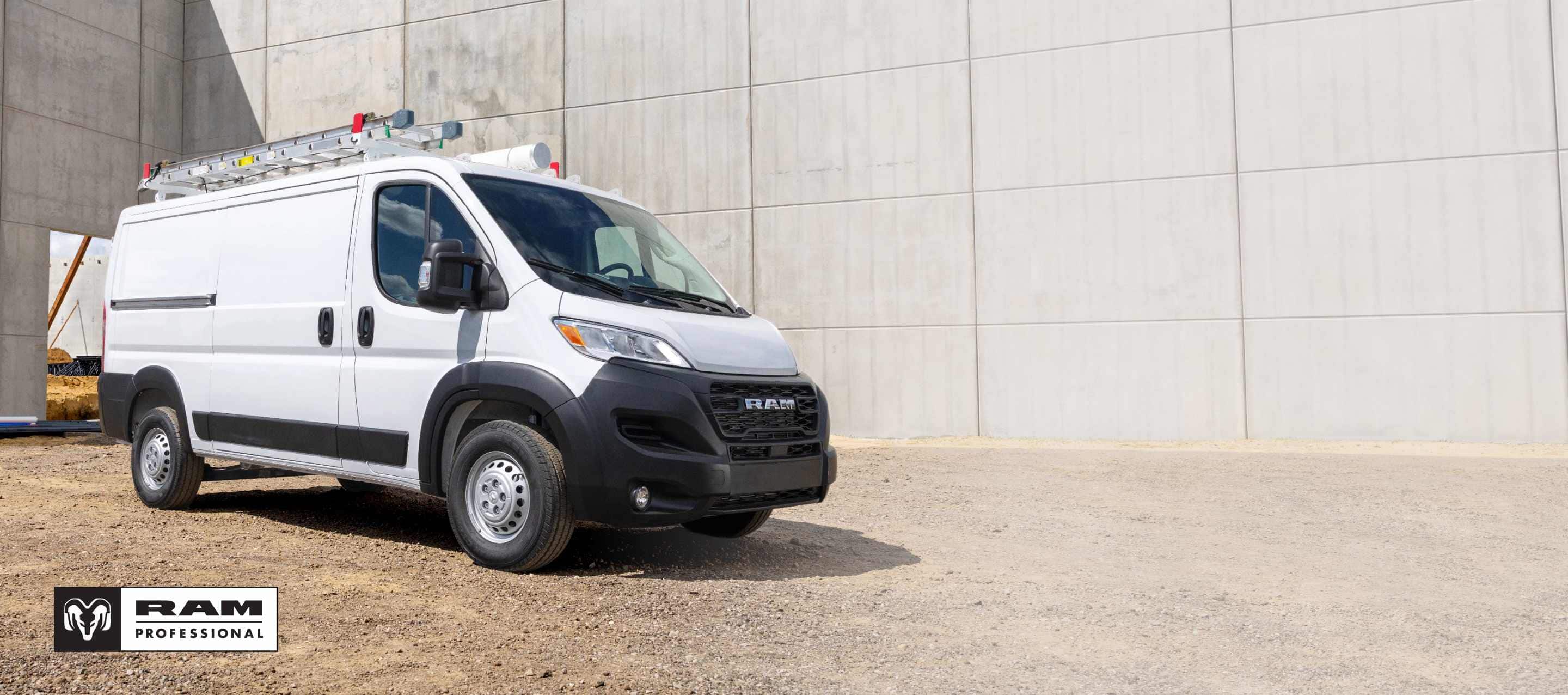 A passenger-side front angle of a white 2025 Ram ProMaster 1500 Tradesman Standard Roof Cargo Van parked at a construction site. Ram Professional.