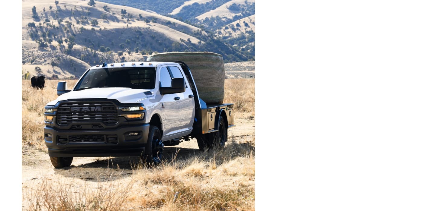 A white 2026 Ram 3500 Tradesman 4x2 Chassis Cab Crew Cab parked on a cattle ranch, carrying a bale of hay on a platform upfit.