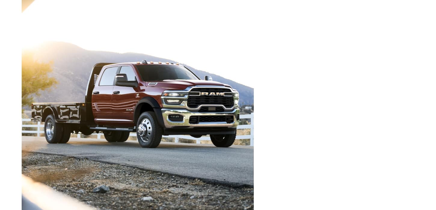 A red 2026 Ram 4500 Big Horn Chassis Cab Crew Cab with a long platform upfit traveling down a road with white picket fences on both sides.