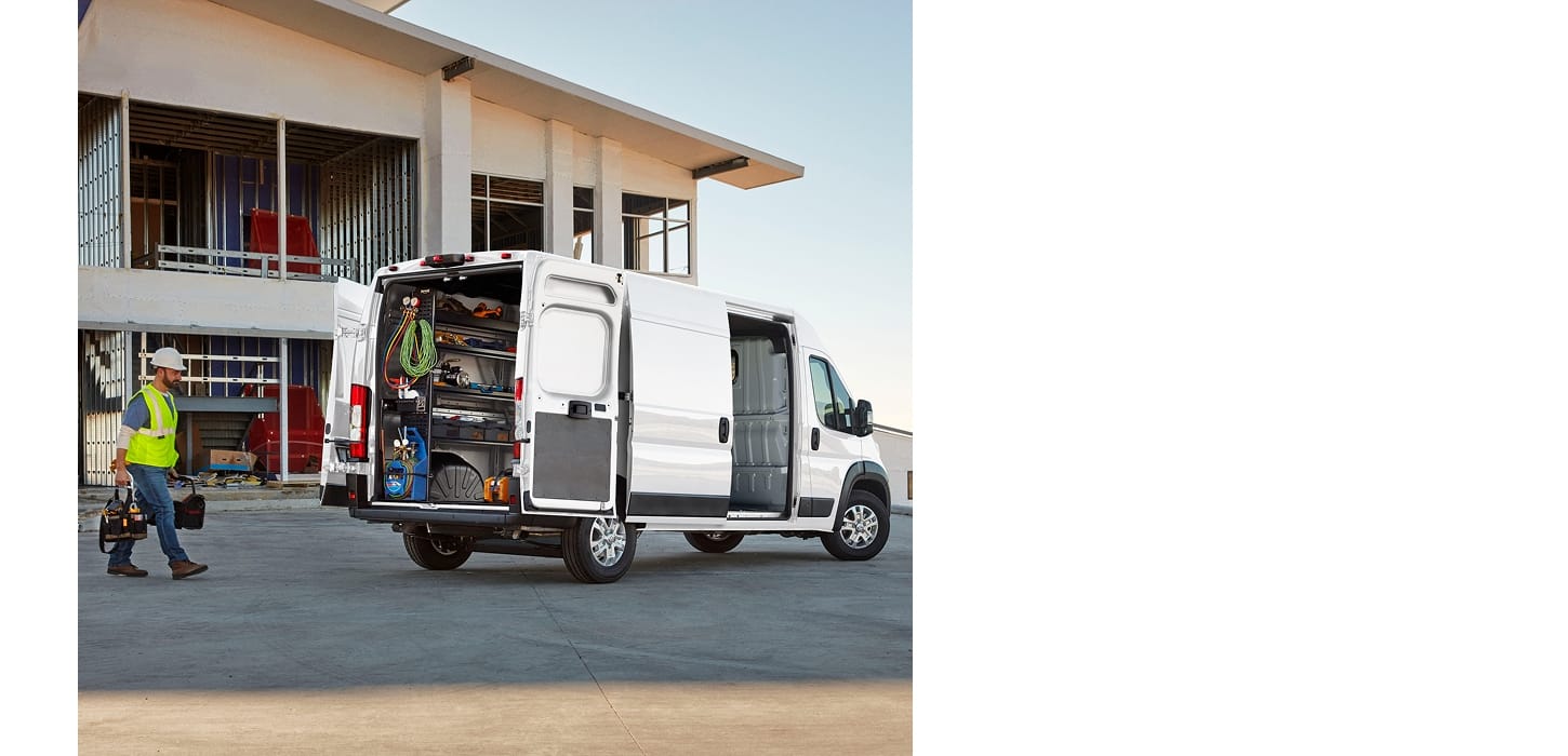 The rear of a white 2026 Ram ProMaster 3500 SLT High Roof Cargo Van with its passenger-side sliding door and rear doors open, displaying shelves full of tools and a technician walking toward the van.