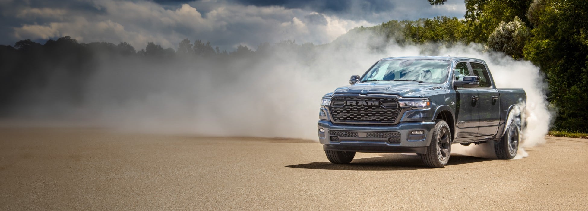 A blue 2026 Ram 1500 Big Horn 4x4 Crew Cab on a clearing, with smoke billowing from its rear tires.