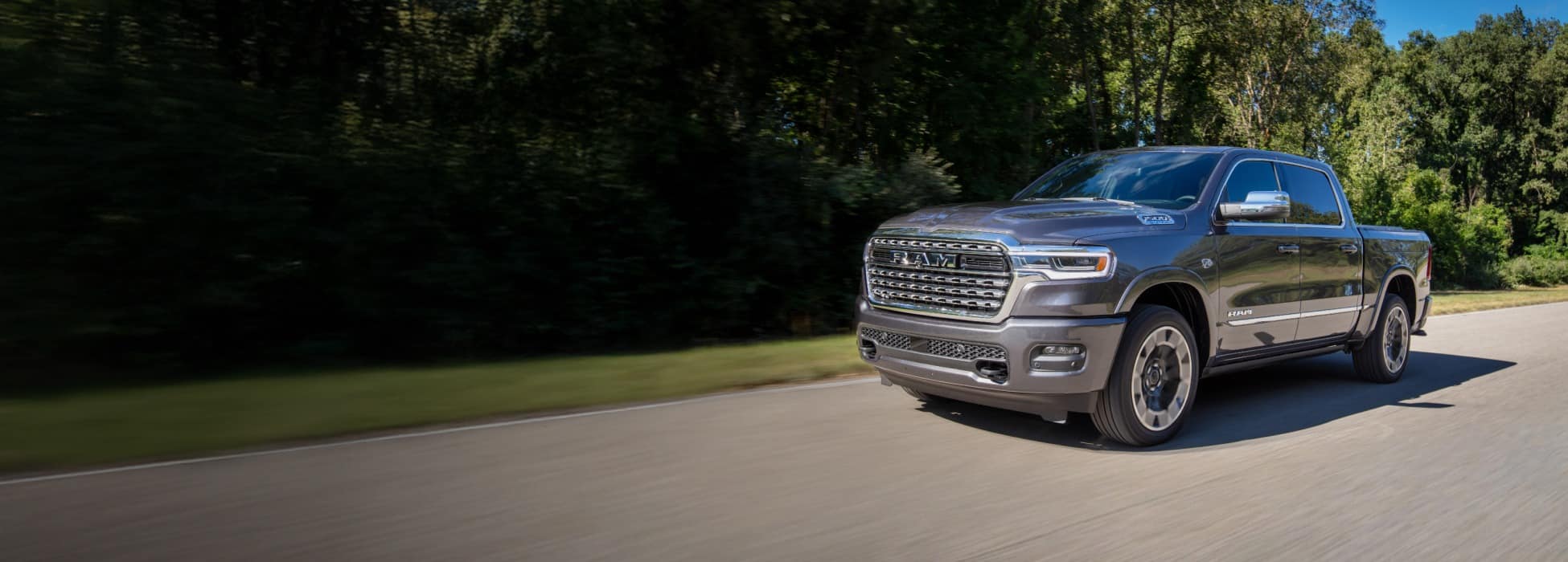 A gray 2026 Ram 1500 Limited 4x4 Crew Cab traveling down a country road.