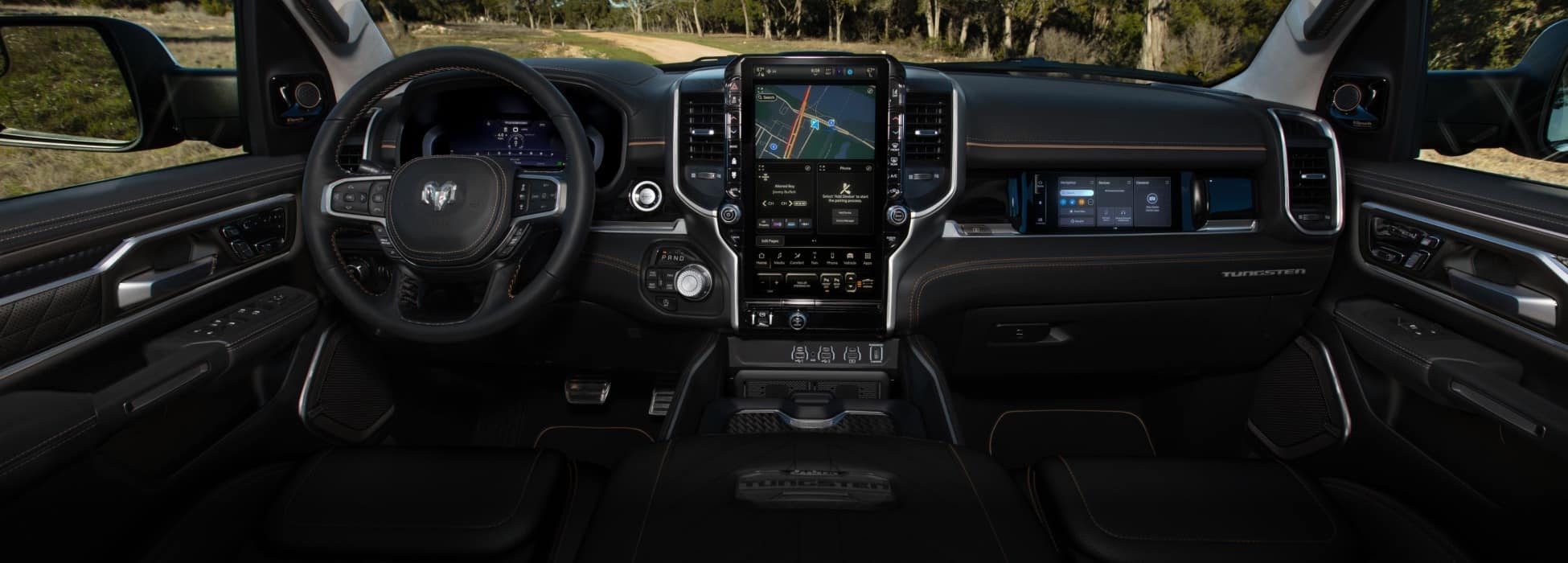 The front seat area in the 2026 Ram 1500 Tungsten, highlighting the steering wheel, Digital Cluster Display, Uconnect touchscreen and Front Passenger Interactive Display.