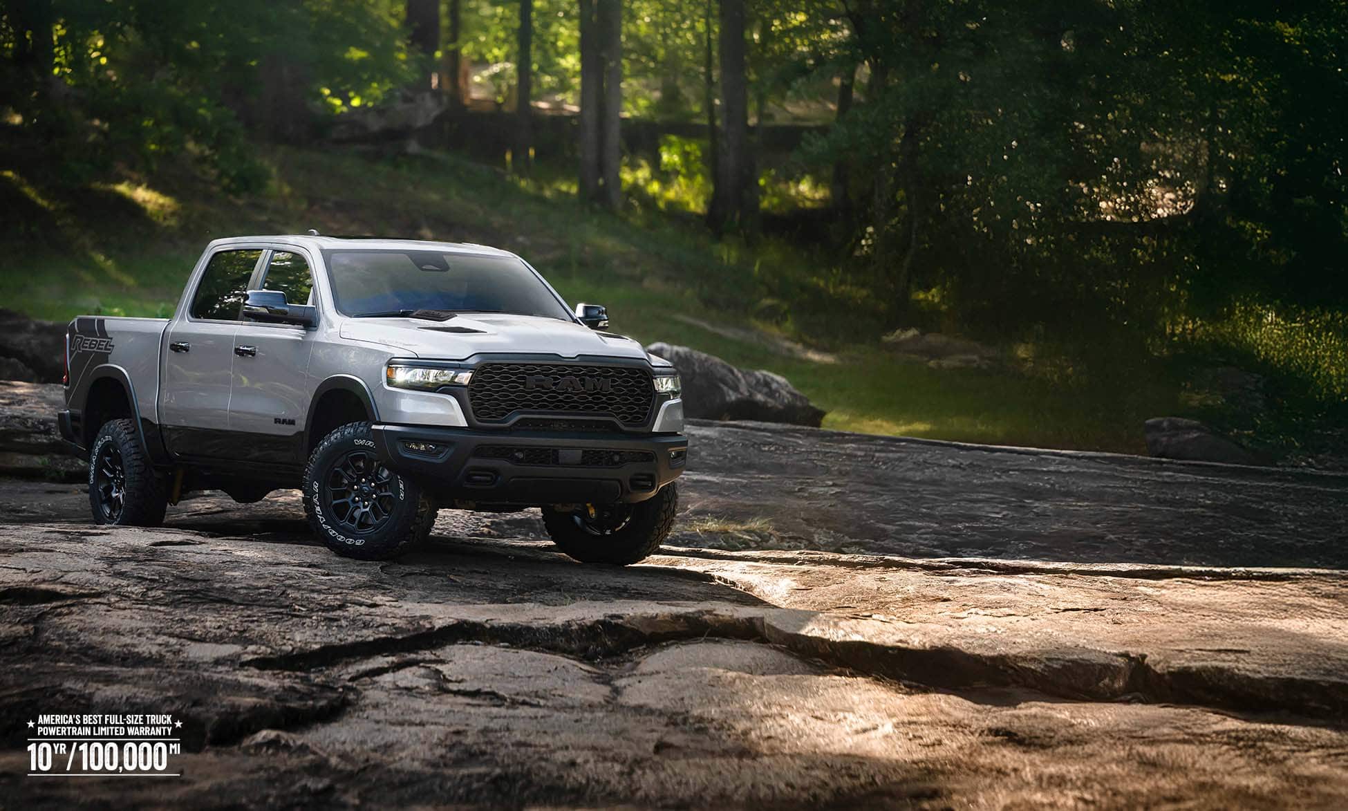 A silver 2026 Ram 1500 Rebel 4x4 Crew Cab traveling across an uneven trail off-road. America’s best full-size truck powertrain limited warranty 10yr/ 100,000mi.