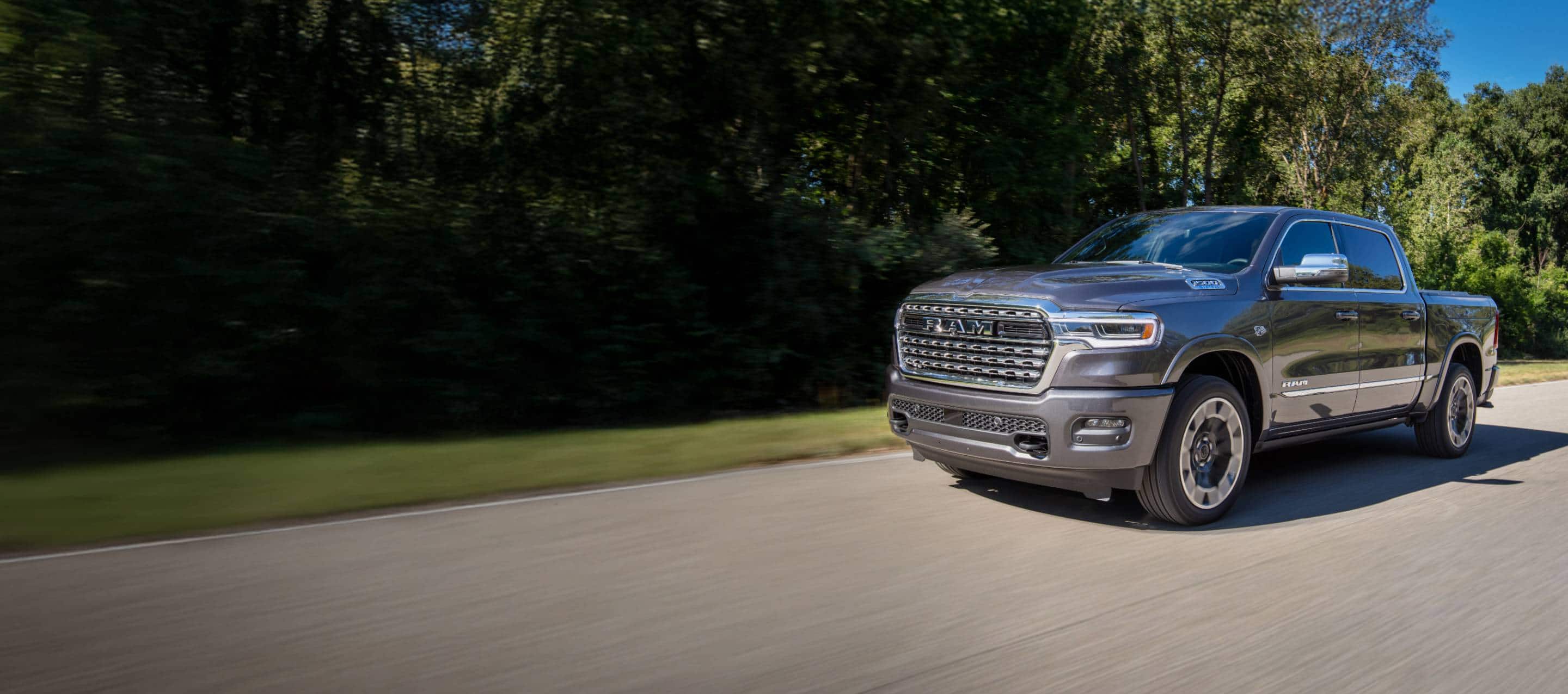 A gray 2026 Ram 1500 Limited 4x4 Crew Cab traveling down a country road. Labor Day Sales Event and 10YR/100000mi.