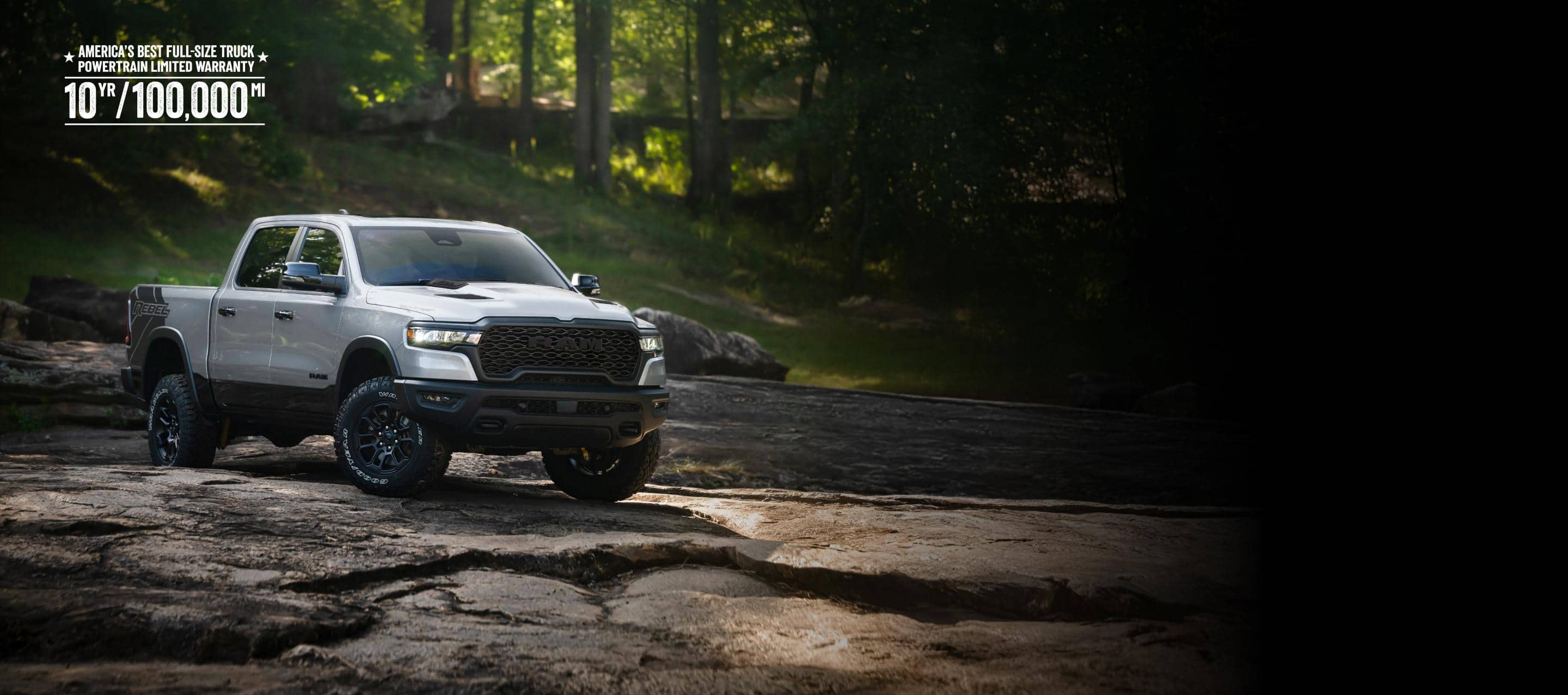 A white 2026 Ram 1500 Rebel 4x4 Crew Cab traveling down a rocky trail off-road, with a forest in the background. America's Best Full-Size Truck Powertrain Limited Warranty. 10-Year, 100,000-Mile.