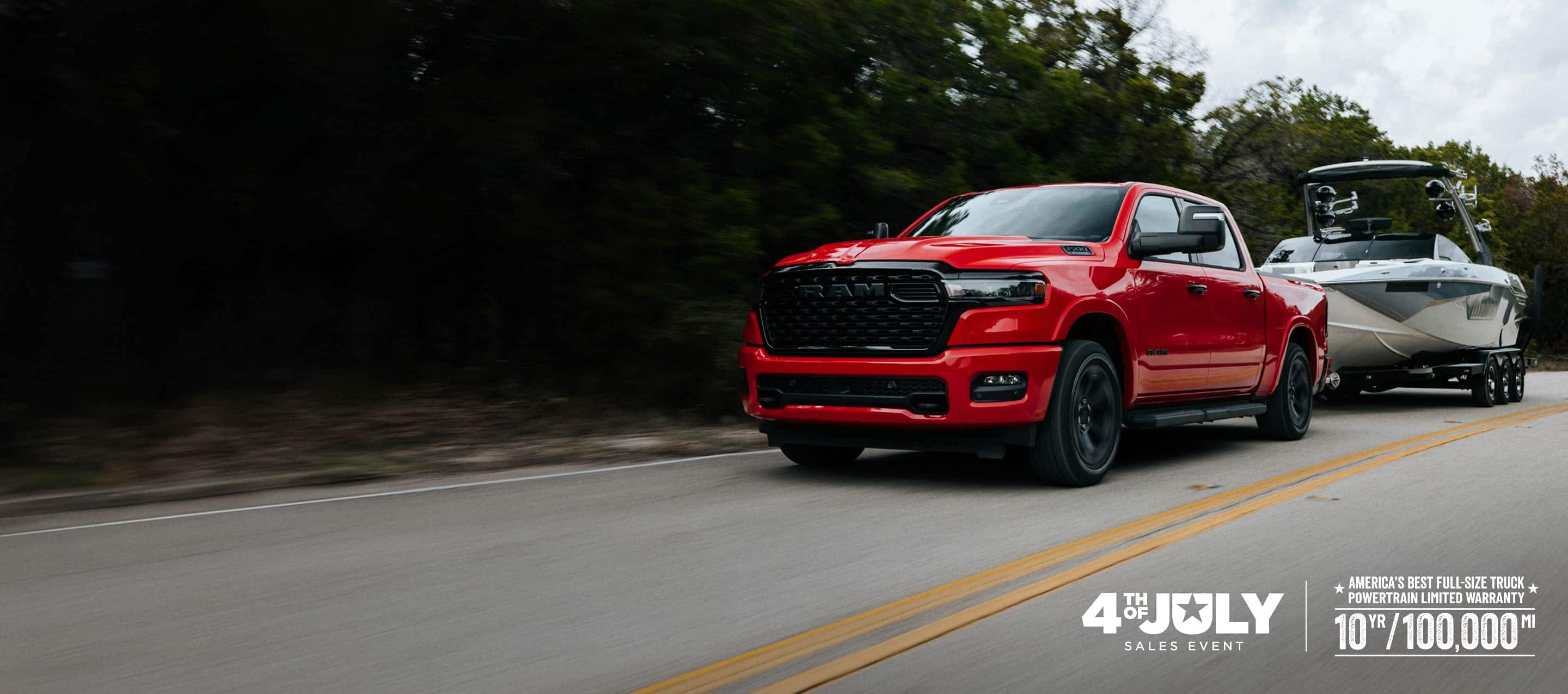 A red 2026 Ram 1500 Big Horn 4x4 Crew Cab pickup traveling down a highway, towing a motorboat. Limited Warranty—10 Years/100,000 Miles. 4th of July Sales Event.