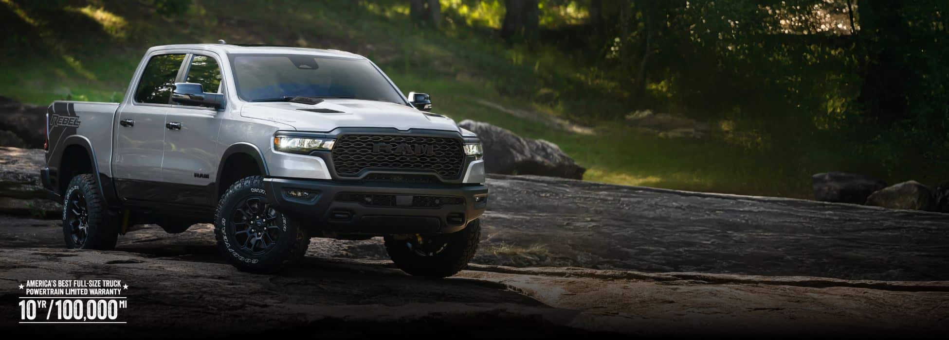 A silver 2026 Ram 1500 Rebel 4x4 Crew Cab traveling across an uneven trail off-road. America’s best full-size truck powertrain limited warranty 10yr/ 100,000mi.