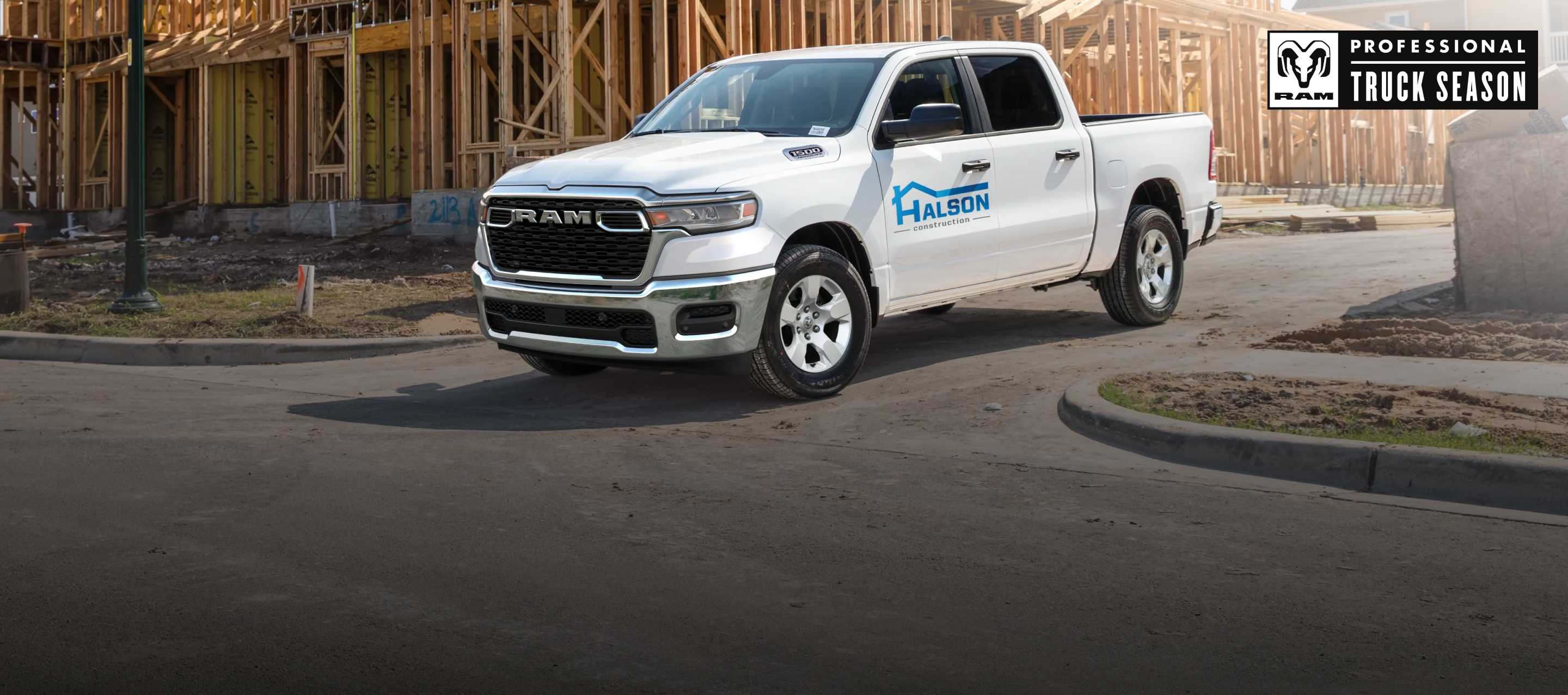  A white 2026 Ram 1500 Tradesman 4x4 Crew Cab, with construction company signage on its driver's door as it pulls away from a commercial building site. Ram Professional Truck Season.