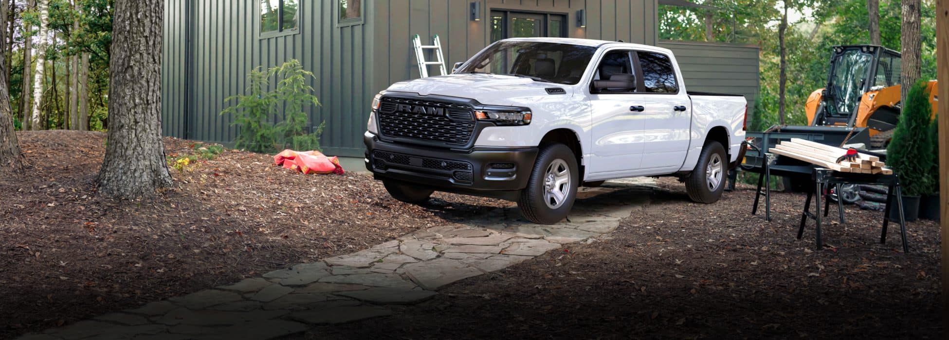 A white 2026 Ram 1500 Tradesman 4x4 Crew Cab parked beside a cabin in the woods.