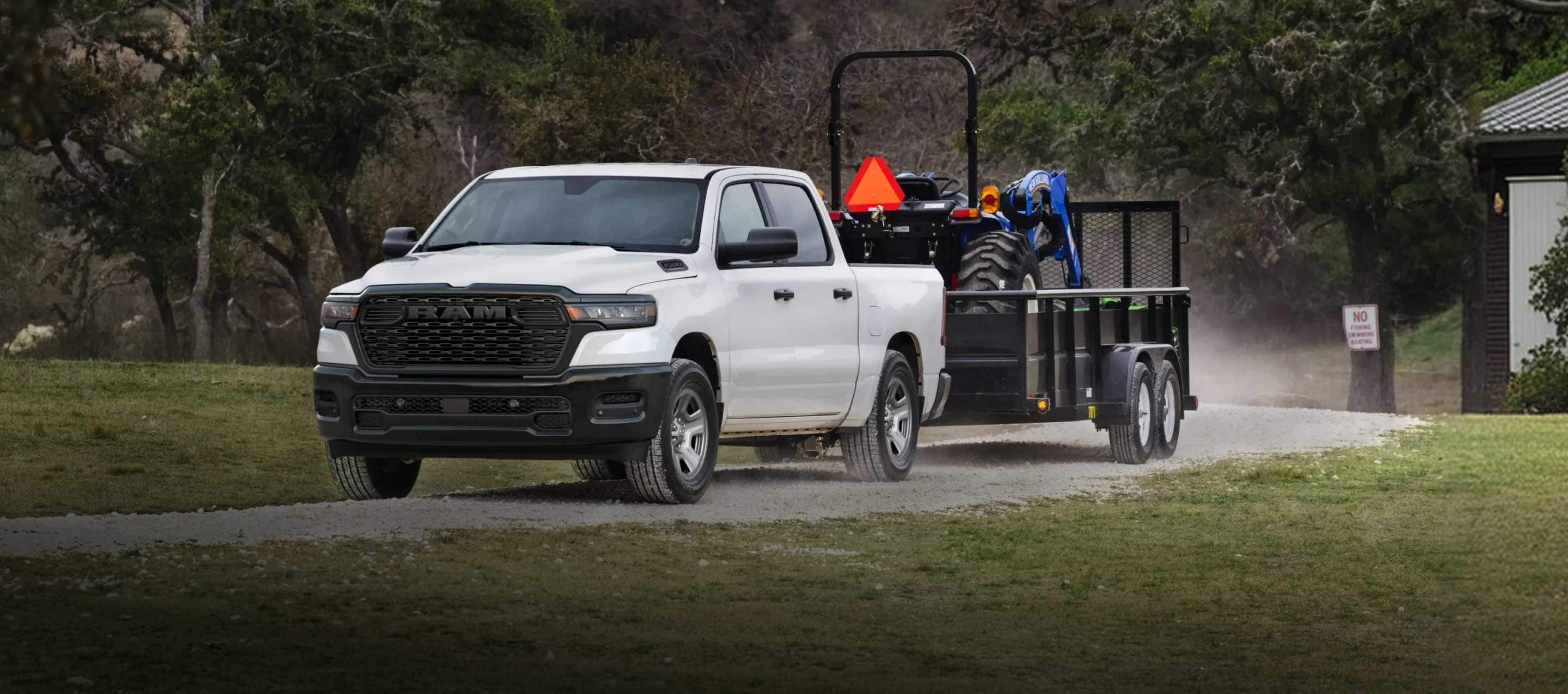 A white 2026 Ram 1500 Tradesman 4x4 Crew Cab towing a tractor on a landscape trailer.