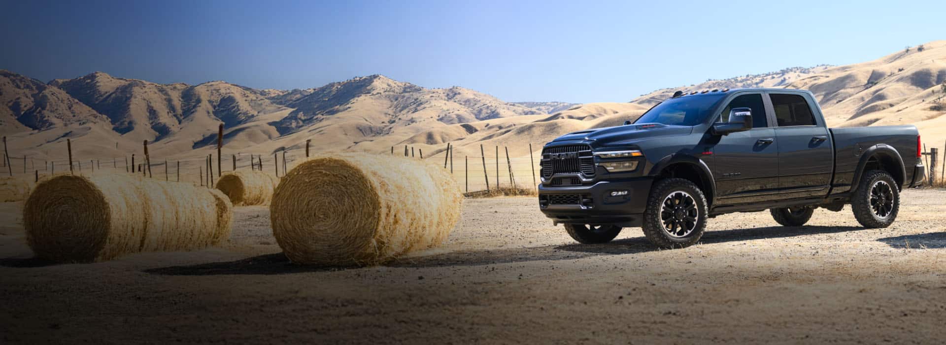 A driver-side front angle of a gray 2025 Ram 2500 Rebel 4x4 Crew Cab parked at a ranch in the desert.