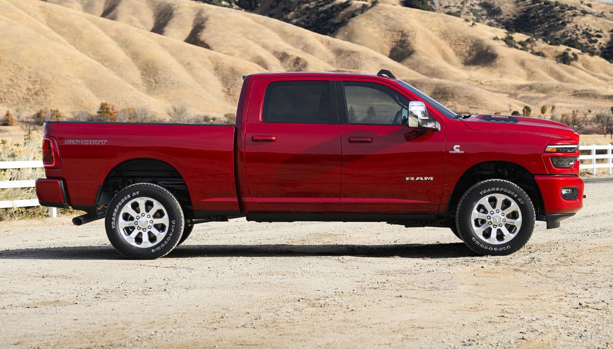 Display A passenger-side profile of a red 2026 Ram 2500 Laramie at a ranch in the desert.