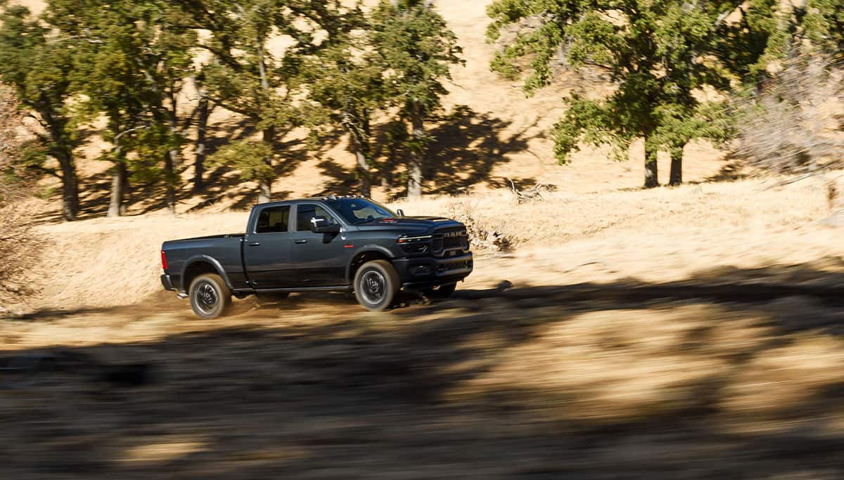 Display A dark gray 2026 Ram 2500 Rebel traveling off-road in the desert. The background is blurred to indicate the truck is in motion.