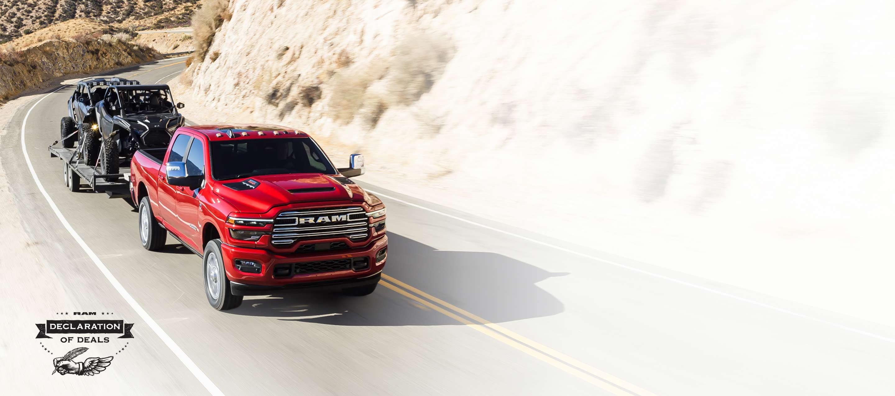 A red 2026 Ram 2500 Laramie 4x4 Crew Cab traveling on a highway in the mountains, while towing two ATVs. Declaration of Deals Sales Event.