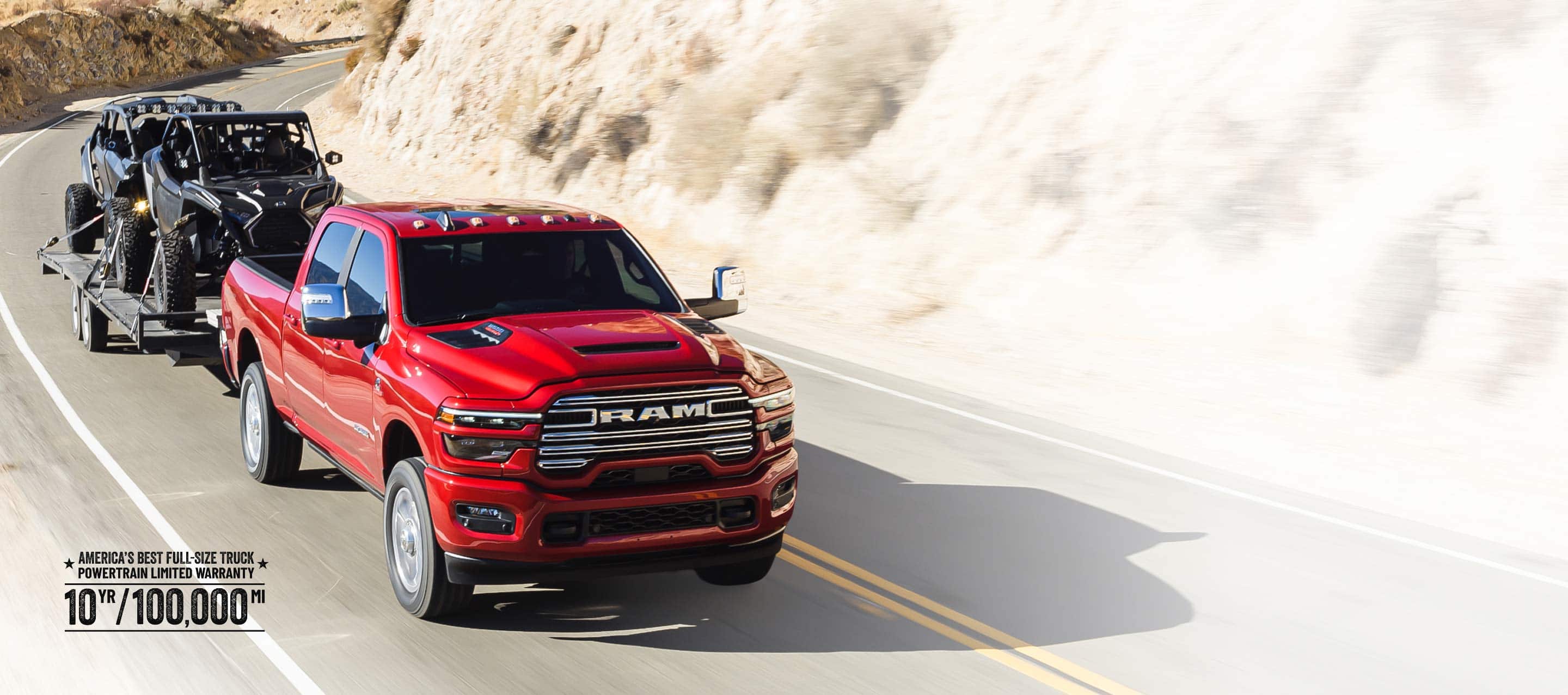 A red 2026 Ram 2500 Laramie 4x4 Crew Cab traveling on a highway in the mountains, while towing two ATVs. Limited Warranty 10yr/ 100,000mi.