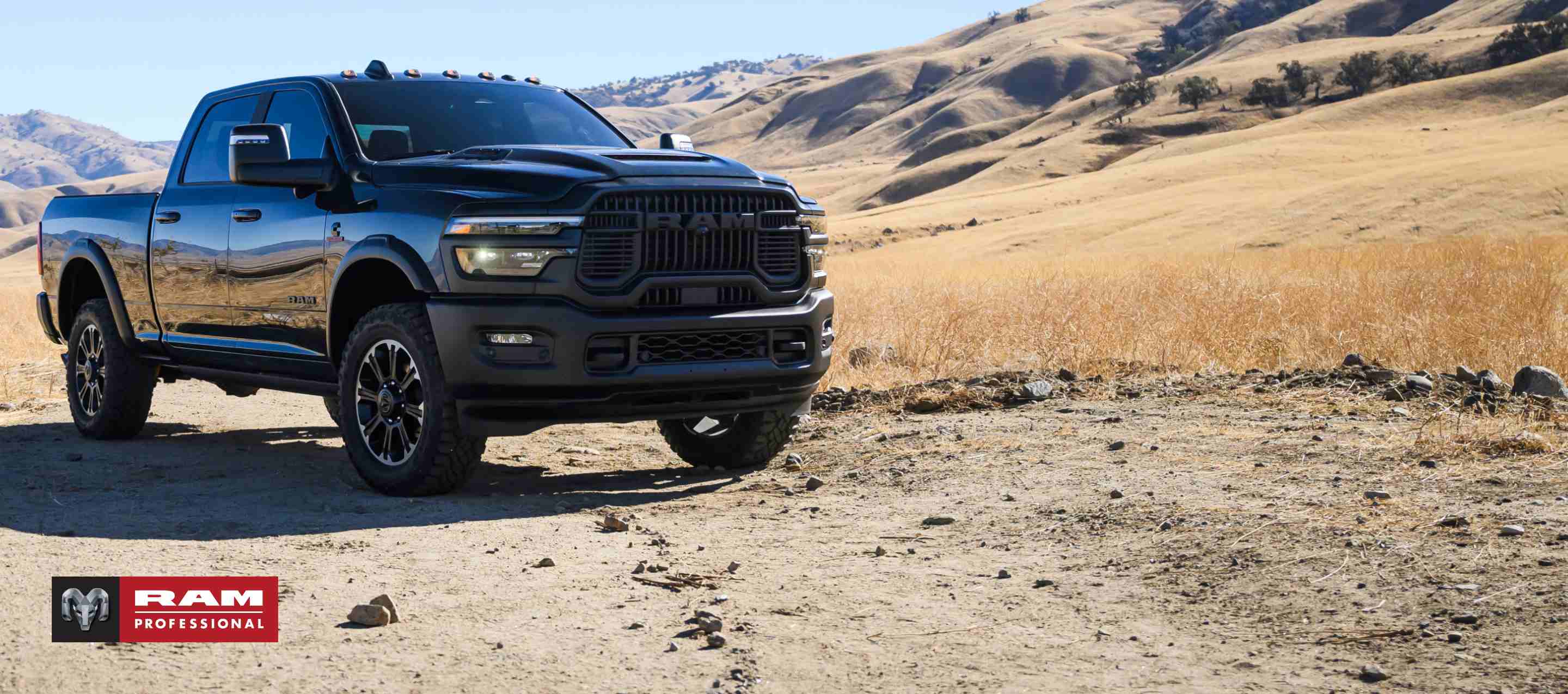 A passenger-side front angle of a black 2026 Ram 2500 Rebel at a desert ranch. Ram Professional.