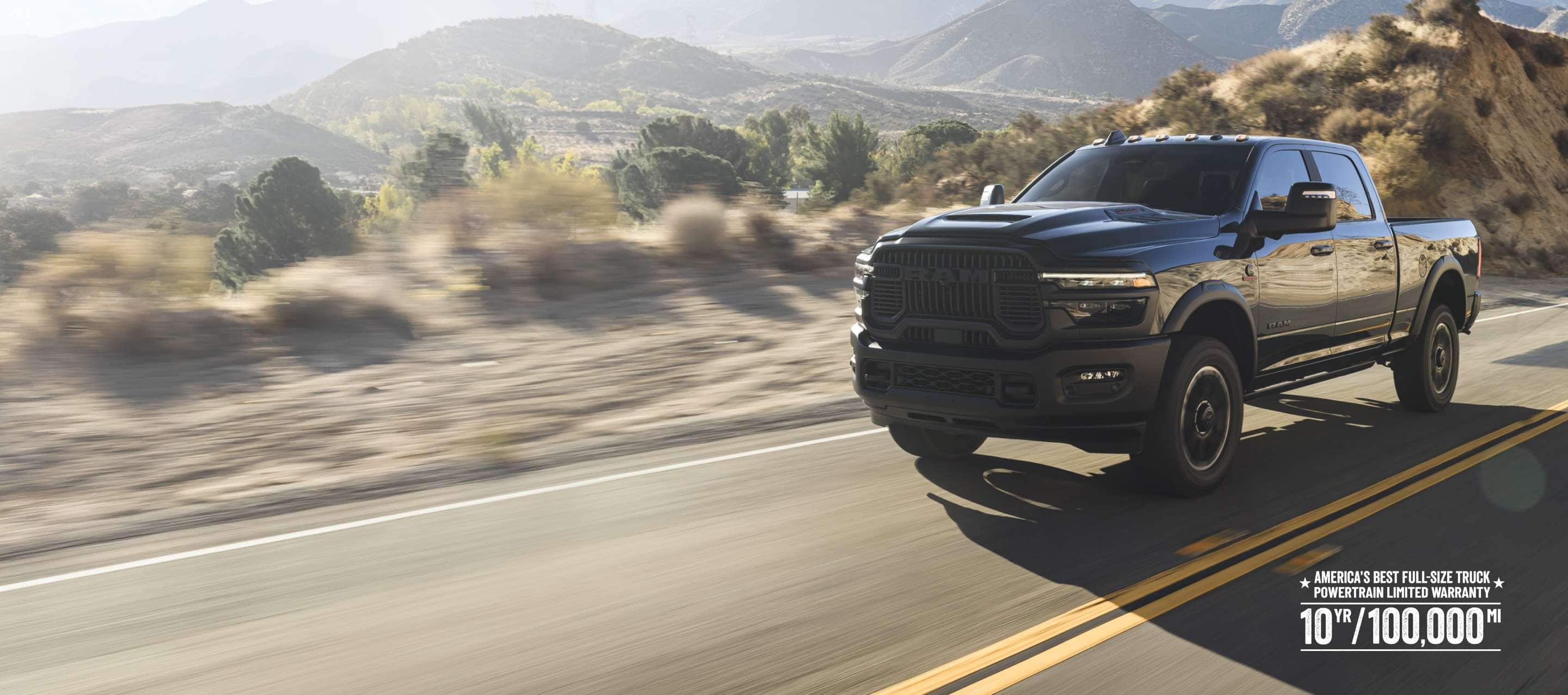 A black 2026 Ram 2500 Rebel traveling on a highway in the desert. The background is blurred to indicate the truck is in motion. America’s best full-size truck powertrain limited warranty 10yr/ 100,000mi.