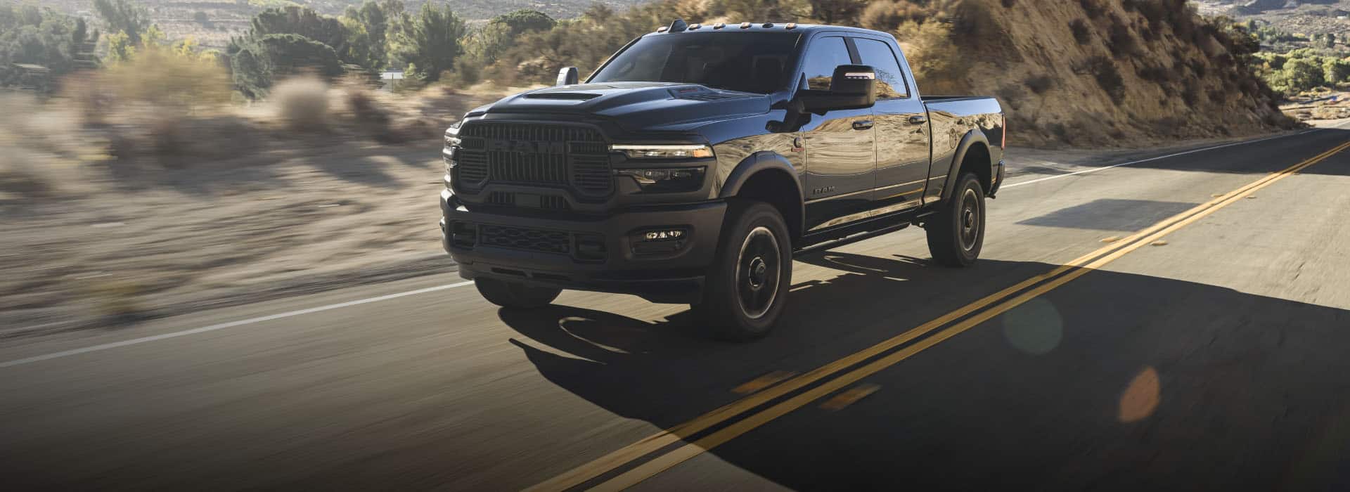 A black 2026 Ram 2500 Rebel traveling on a highway in the desert. The background is blurred to indicate the truck is in motion.