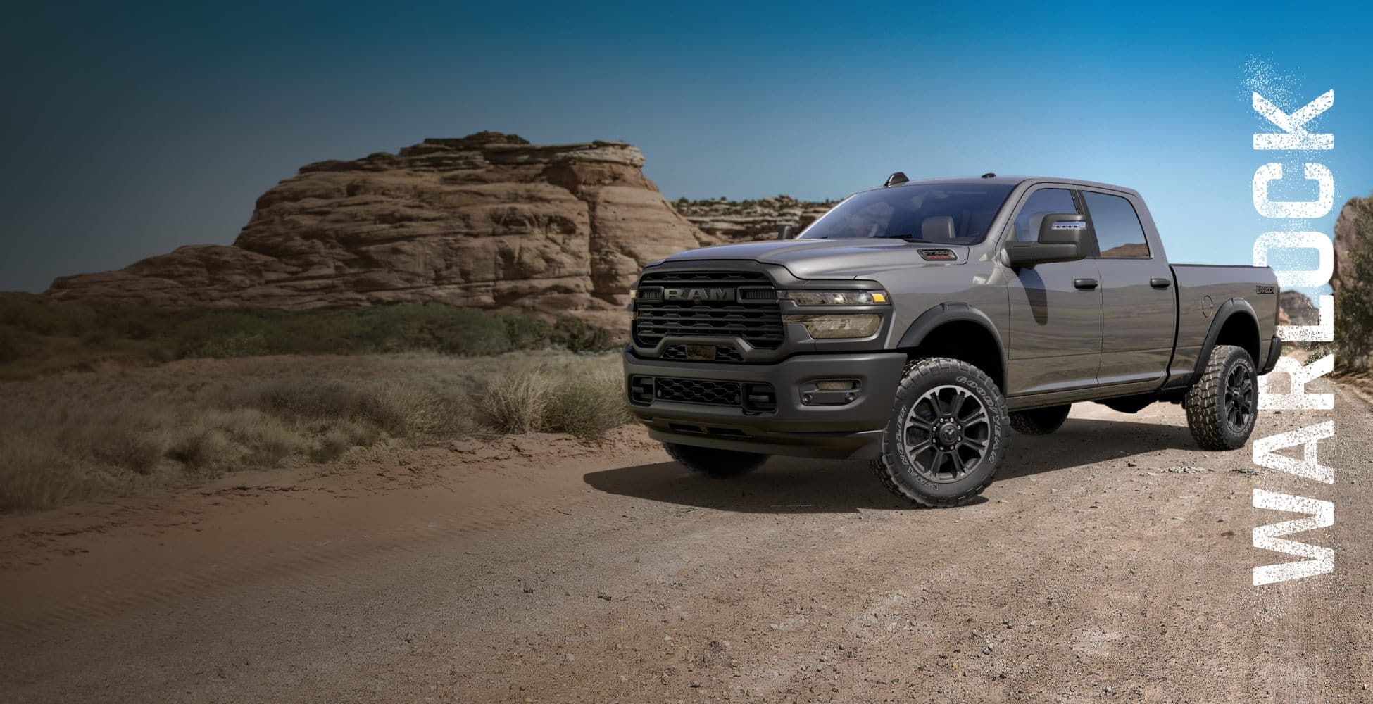 An angled driver-side profile of a gray 2026 Ram 2500 Warlock Crew Cab parked on a trail off-road in the desert. Warlock.