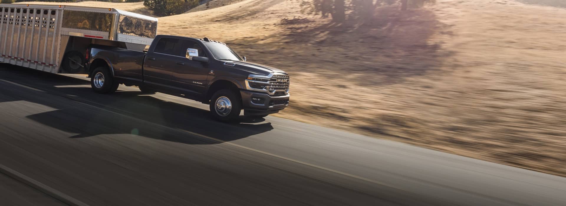 A black 2026 Ram 3500 Limited Longhorn Crew Cab towing a large fifth-wheel livestock trailer as it travels down a highway.