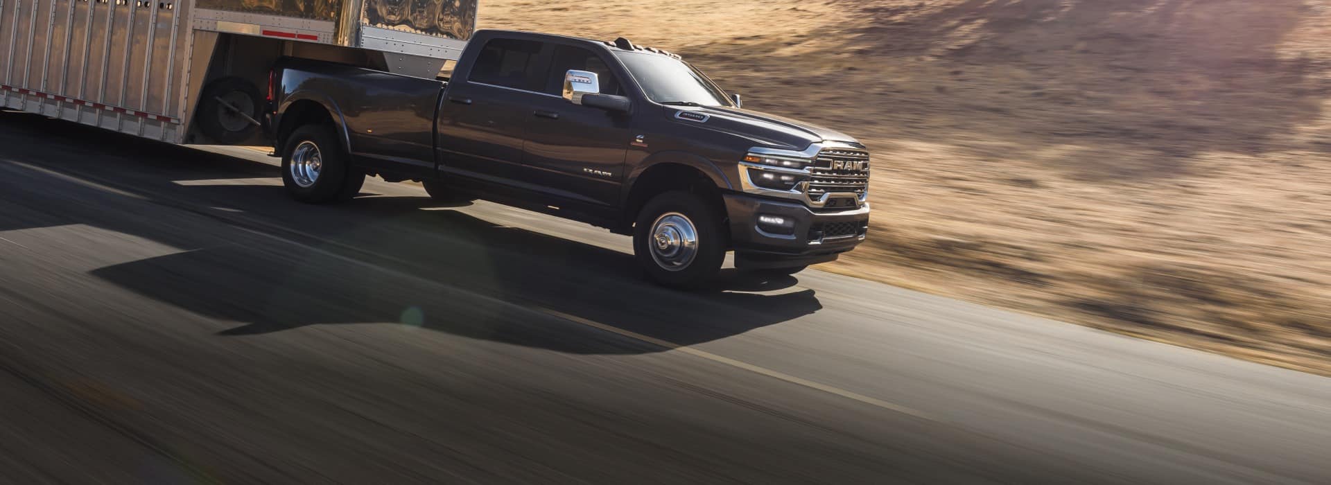 A black 2026 Ram 3500 Limited Longhorn Crew Cab towing a large fifth-wheel livestock trailer as it travels down a highway.