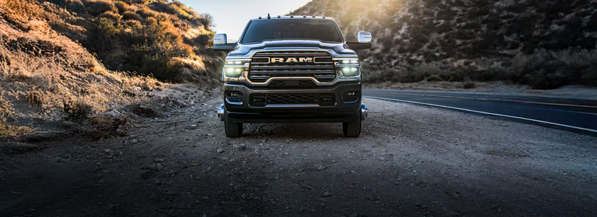 A head-on angle of a blue 2026 Ram 3500 Limited parked on the shoulder of a highway in the mountains.