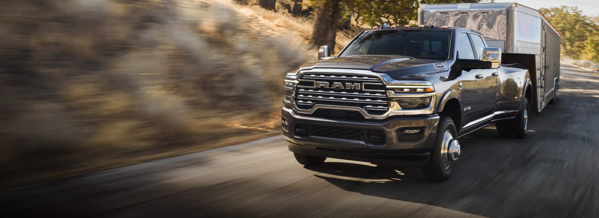A gray 2026 Ram 3500 Limited Longhorn 4x4 Crew Cab towing a large fifth-wheel livestock trailer as it travels down a highway. The background is blurred to indicate the truck is in motion.