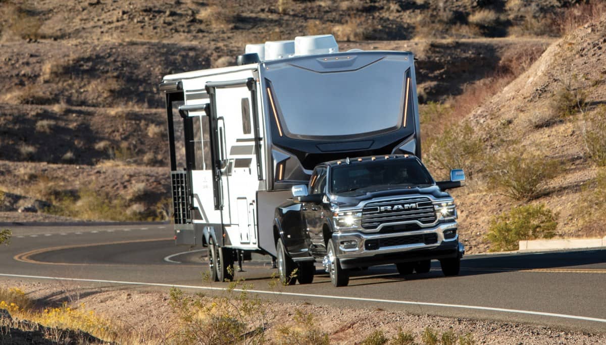 Display A black 2026 Ram 3500 traveling on a mountain highway, towing an RV.