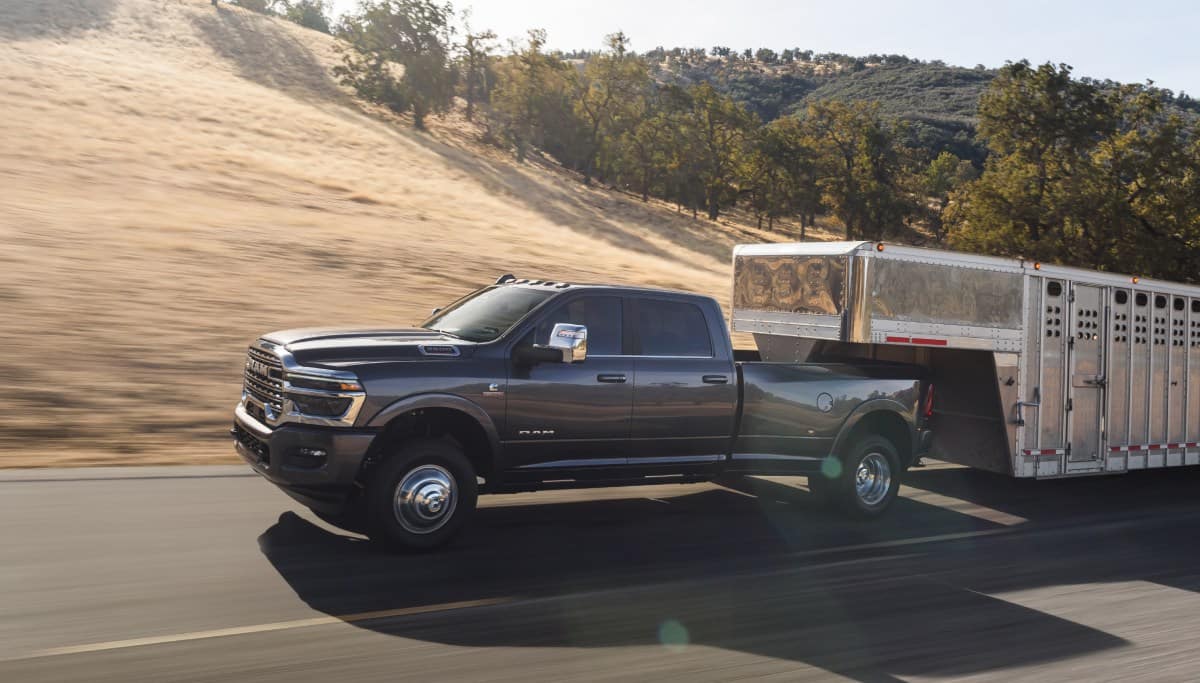 Display A gray 2026 Ram 3500 Limited Longhorn 4x4 Crew Cab towing a large fifth-wheel livestock trailer as it travels down a highway.