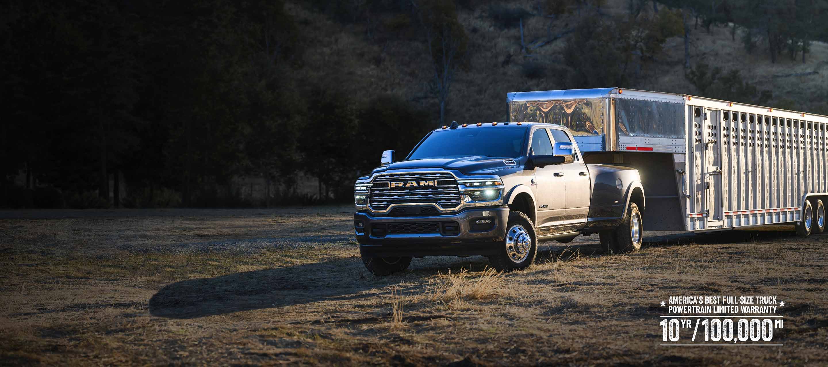 A gray 2026 Ram 3500 Limited Longhorn 4x4 Crew Cab towing a large fifth-wheel livestock trailer as it travels off-road. Limited warranty 10yr/ 100,000mi.