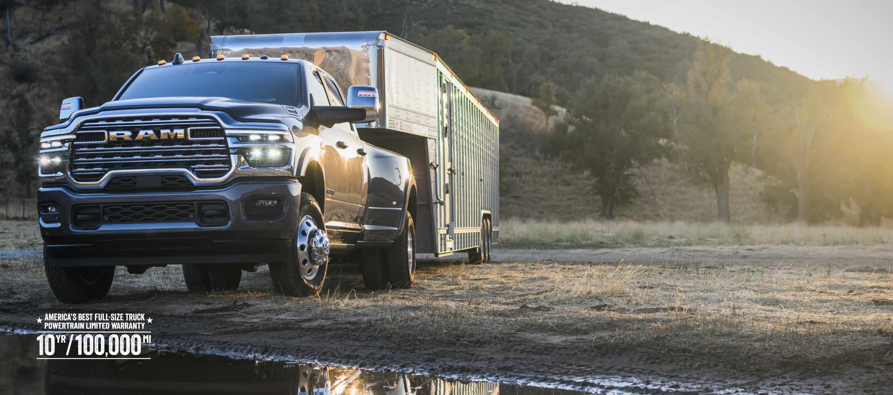 A black 2026 Ram 3500 Limited Longhorn 4x4 Crew Cab towing a large fifth-wheel livestock trailer off-road, beside a waterfront. America’s best full-size truck powertrain limited warranty 10yr/ 100,000mi.