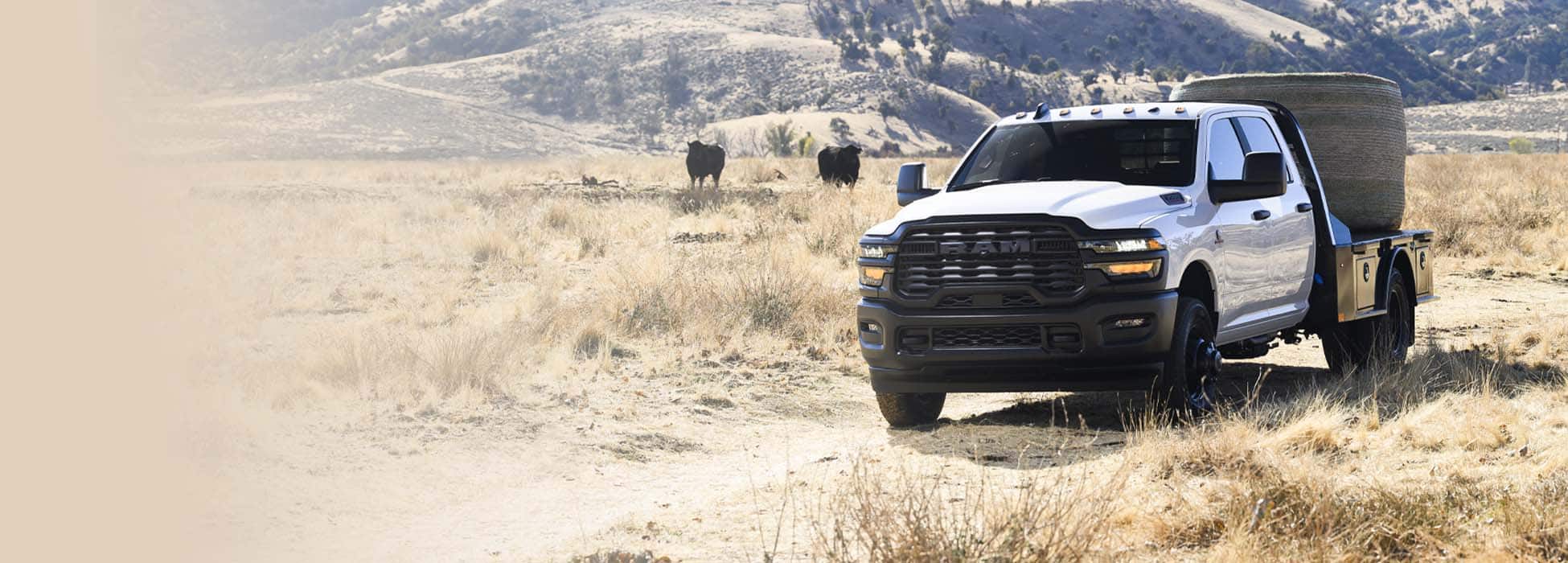 A white 2026 Ram 3500 Tradesman 4x2 Chassis Cab Crew Cab parked on a cattle ranch, carrying a bale of hay on a platform upfit.