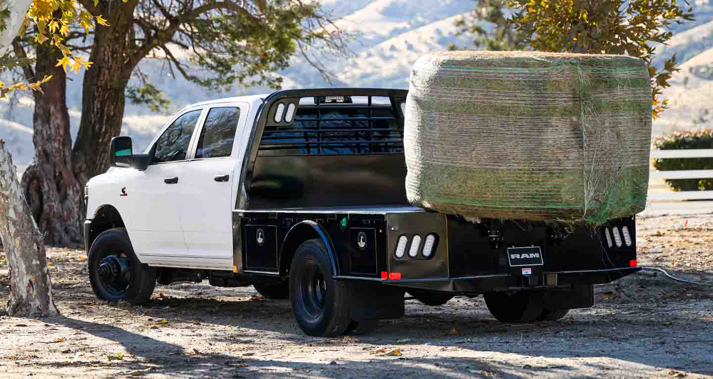 Display A white 2026 Ram 3500 Tradesman Chassis Cab Crew Cab with a huge bale of hay on its platform upfit, parked at a farm.