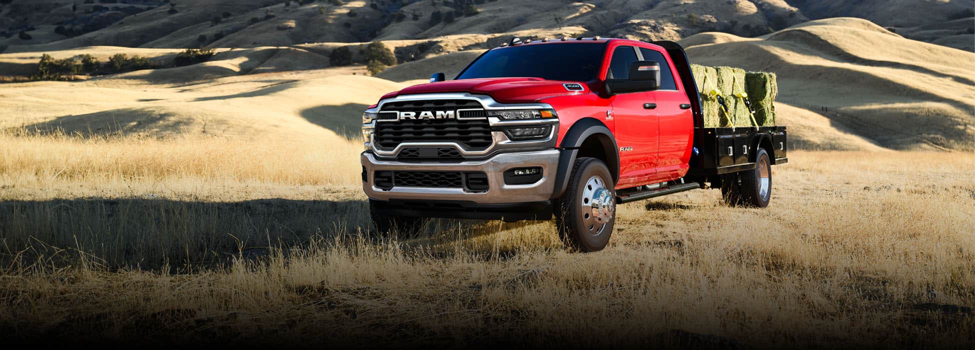 A red 2026 Ram 5500 Laramie Chassis Crew Cab carrying several large bales of hay on a long platform upfit.