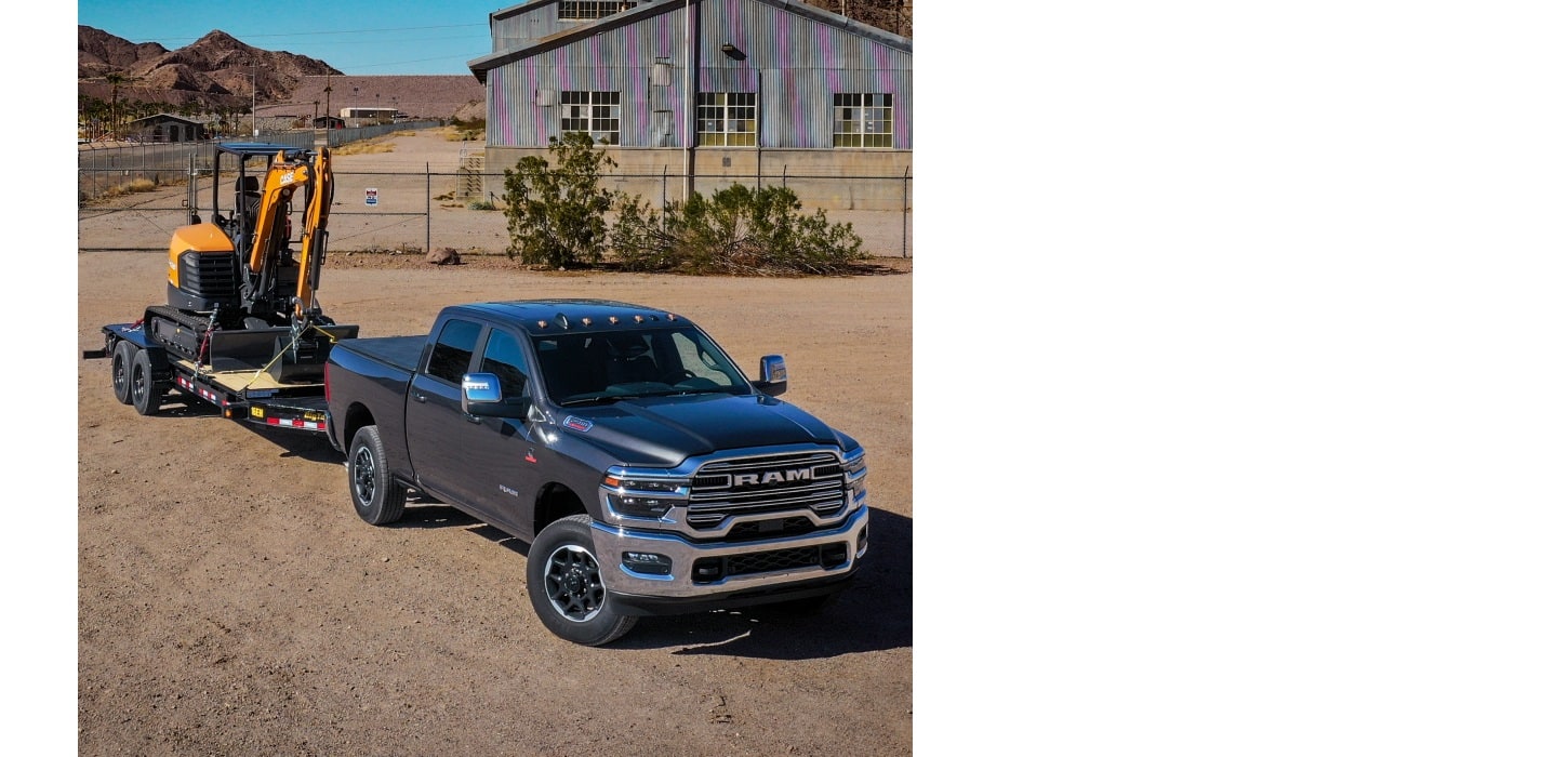 A gray 2025 Ram 2500 Laramie 4x4 Crew Cab at a cattle ranch, towing an excavator on a flatbed trailer.