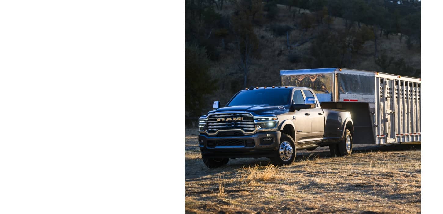 A gray 2026 Ram 3500 Limited Longhorn 4x4 Crew Cab towing a large fifth-wheel livestock trailer off-road.
