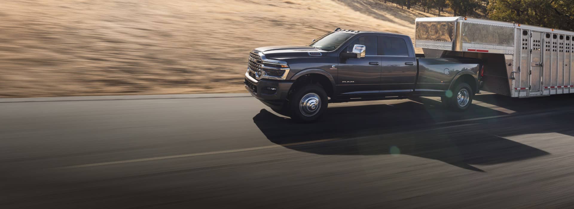 A 2026 Ram 3500 Limited Longhorn 4x4 Crew Cab towing a large fifth-wheel livestock trailer and a black 2026 Ram 2500 Rebel 4x4 Crew Cab parked near each other.