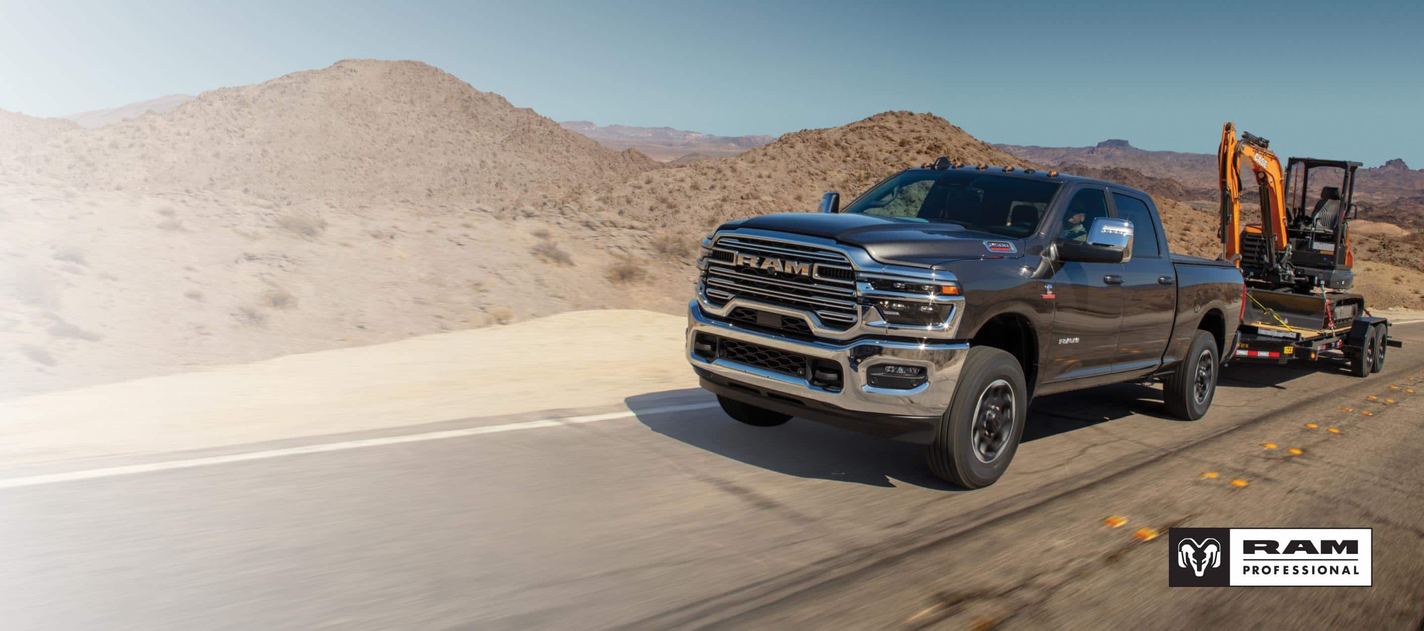 A black 2026 Ram 2500 Laramie 4x4 Crew Cab traveling down a highway, towing an excavator on a flat bed trailer. Ram Professional.