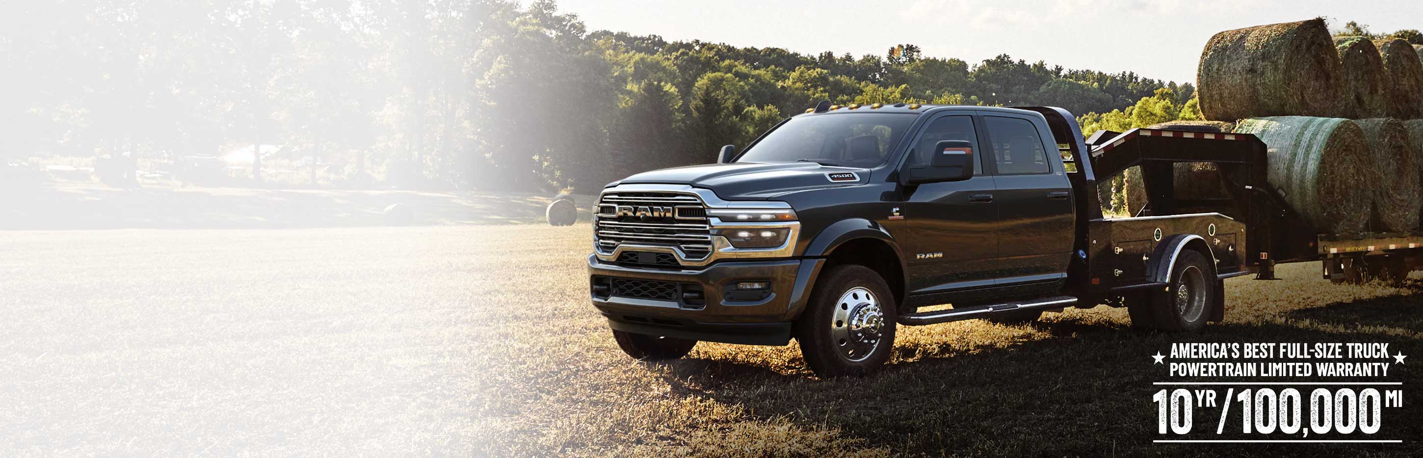 A black 2026 Ram 4500 Big Horn Chassis Cab Crew Cab with the Laramie Trim Group and a gooseneck trailer loaded with several large bales of hay, parked in an open field. America's Best Full-Size Truck Powertrain Limited Warranty. 10 Year/100,000 Mile.