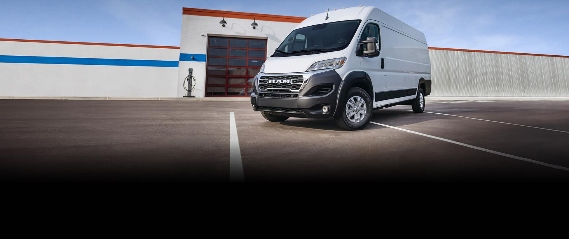 A driver-side front angle of a white 2026 Ram ProMaster EV 3500 SLT Plus High Roof Cargo Van parked near a commercial garage.