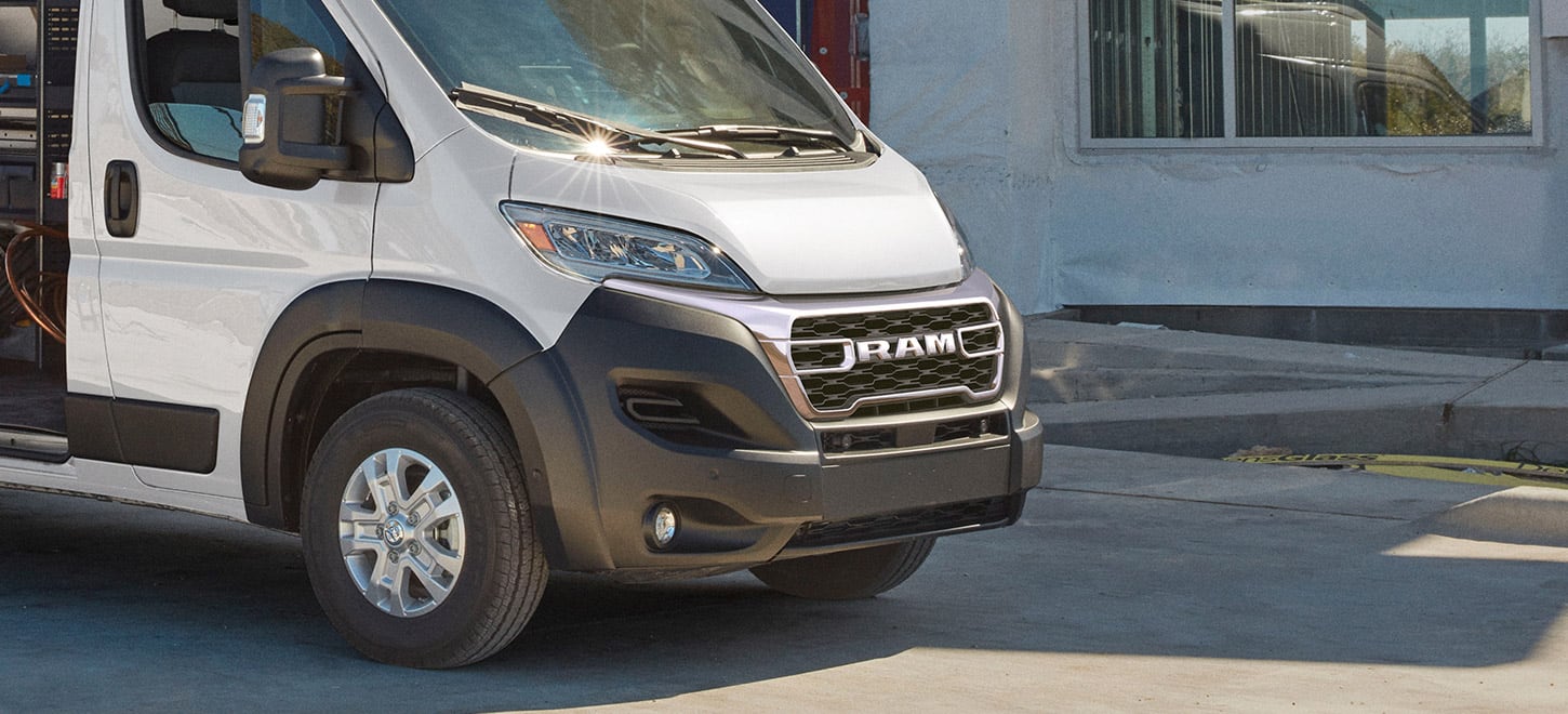 Display A passenger-side front angle of a white 2026 Ram ProMaster 2500 SLT Cargo Van High Roof, parked beside a commercial building.