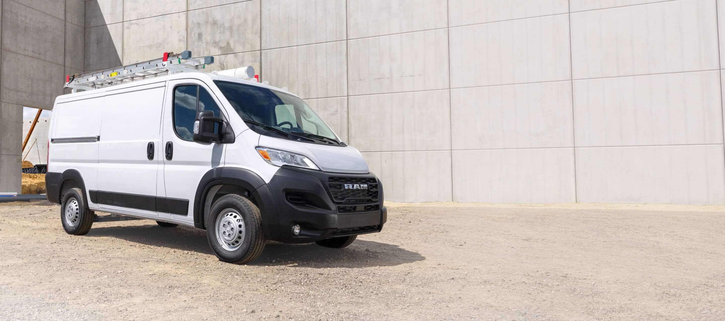 A white 2026 Ram ProMaster Tradesman Standard Roof Cargo Van with a ladder on its roof rack, at a construction site, shot on an angled profile.